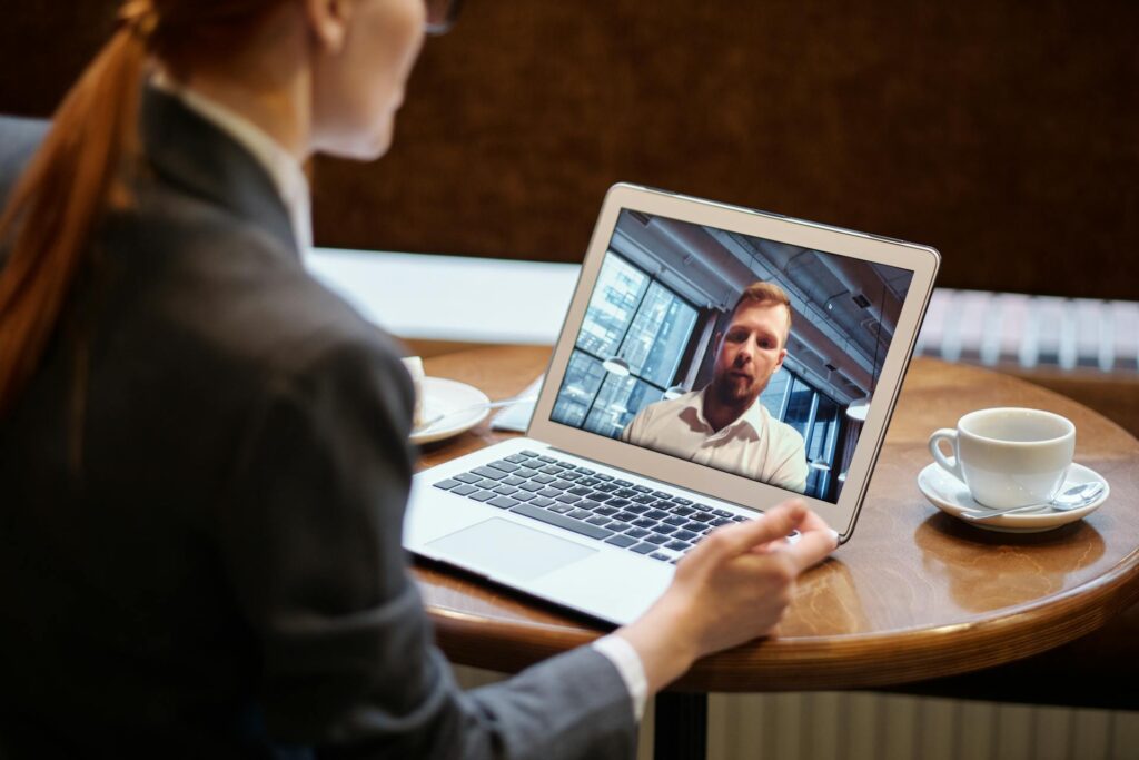 Das Bild steht in Zusammenhang mit Mediation und Konfliktlösung durch die Kanzlei Ponschab & Partner und zeigt folgendes: Eine Person im Anzug sitzt an einem Tisch mit einem Laptop und nimmt an einem Videogespräch mit einer anderen Person auf dem Bildschirm teil. Eine Tasse Kaffee und eine Untertasse stehen auf dem Tisch neben dem Laptop. Bei Fragen zu Konflikten und Konfliktlösung wenden Sie sich bitte an uns unter info@ponschab-partner.com